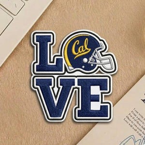 May include: Embroidered patch featuring the word "LOVE" in navy blue block letters with a white border. The "O" is replaced by a navy blue football helmet with "Cal" in yellow. The patch is on a tan surface.