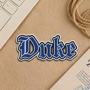 May include: A set of three ceramic mugs with a speckled, cream-colored glaze. Each mug features a different hand-painted design: a blue and green leaf, a yellow flower, and a red berry. The mugs have a simple, modern design.