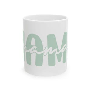 Könnte beinhalten: Weiße Keramiktasse mit dem Wort "MAMA" in großen, hellgrünen Blockbuchstaben, wobei das Wort "mama" in einer Schreibschrift die Blockbuchstaben überlagert. Die Tasse hat eine Standardgröße.