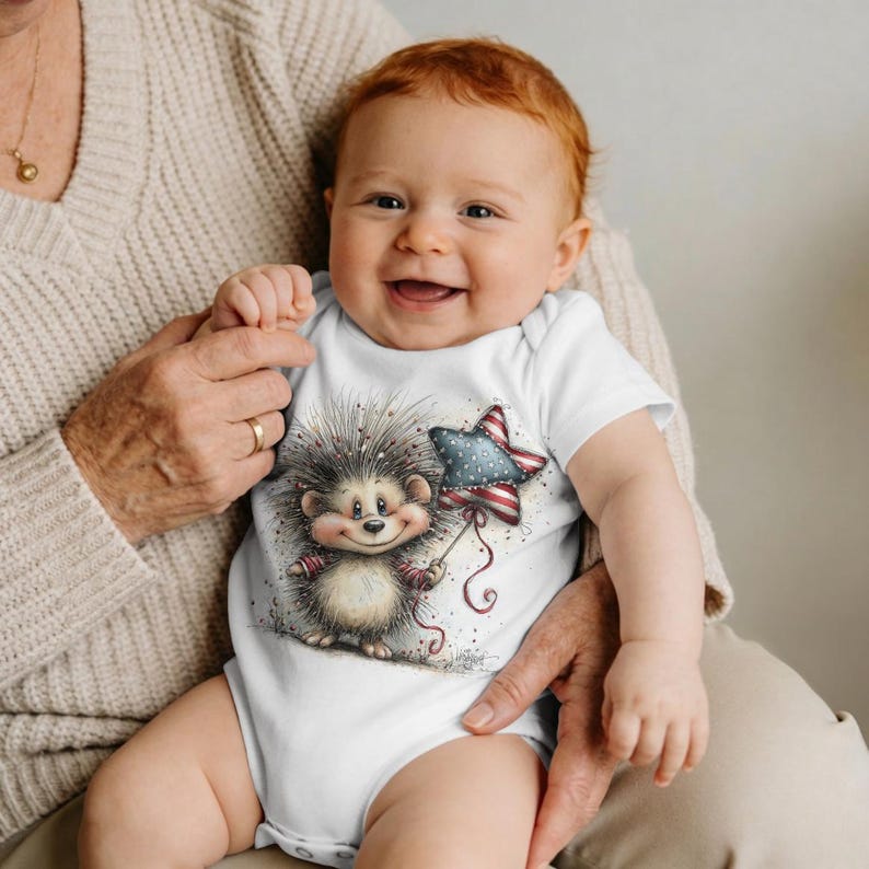 May include: A baby in a white onesie smiles, the garment featuring a cartoon hedgehog holding a star-shaped balloon. The balloon has a red, white, and blue pattern. The baby has red hair and is held by someone wearing a beige sweater.