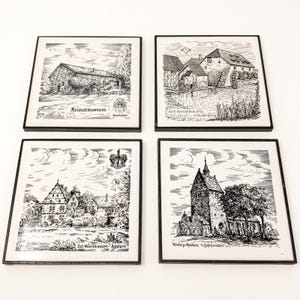 May include: A set of four square coasters with black frames, each featuring a detailed black and white ink illustration of a German building. The designs include the Heimatmuseum, Alte Wassermühle in Rodenberg, Gut Münchhausen-Apelern, and Kirche zu Apelern.