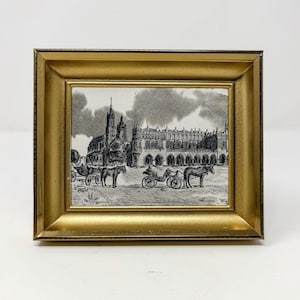May include: A framed black and white ink drawing depicting a historic town square with a large church, arched buildings, and horse-drawn carriages. The artwork is enclosed in a thick, metallic gold-colored frame with a beveled edge design.
