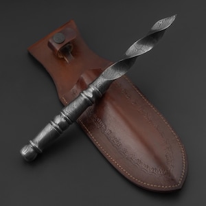 May include: A Damascus steel dagger with a twisted blade rests in a brown leather sheath. The dagger's handle and blade feature a detailed pattern. The sheath has decorative stitching and a belt loop.