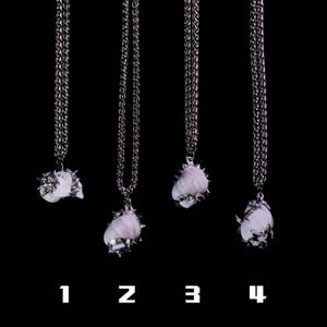 May include: Four silver-toned necklaces with pendant stones in varying shapes and colors, suspended from a chain. The pendants are a mix of white and lavender hues, with a spiky metal setting. The background is solid black, and numbers 1-4 are at the bottom.