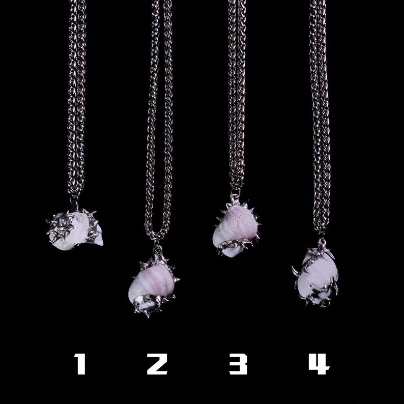 May include: Four silver-toned necklaces with pendant stones in varying shapes and colors, suspended from a chain. The pendants are a mix of white and lavender hues, with a spiky metal setting. The background is solid black, and numbers 1-4 are at the bottom.