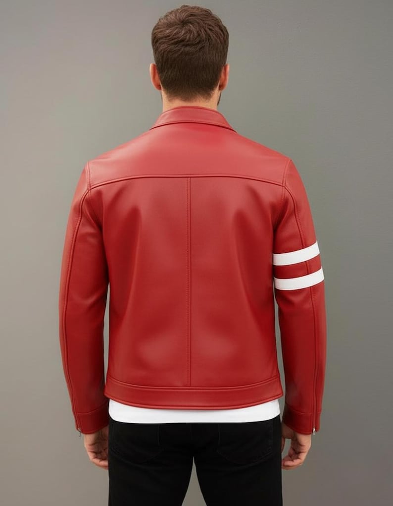 Op de afbeelding: Een rode leren jas met witte strepen op de linkermouw. De jas heeft een klassieke kraag, een verticale naad op de rug en een rits op de mouw. De persoon draagt een wit t-shirt en een zwarte broek.