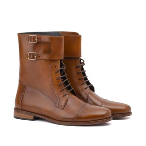 May include: A pair of brown leather boots with a cap toe design. The boots have a lace-up closure and two buckle straps at the top. The boots are approximately 20 cm tall.