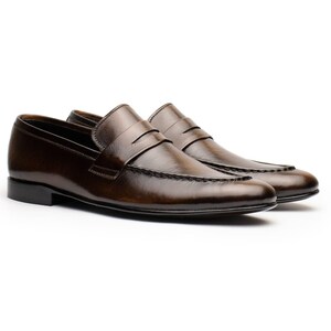 May include: A pair of brown leather penny loafers. The shoes have a classic design with a rounded toe, a strap across the vamp, and a low heel. The leather has a polished finish.