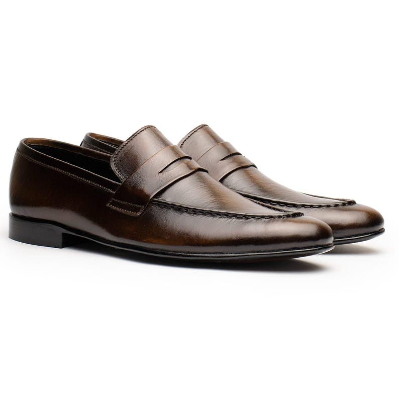 May include: A pair of brown leather penny loafers. The shoes have a classic design with a rounded toe, a strap across the vamp, and a low heel. The leather has a polished finish.