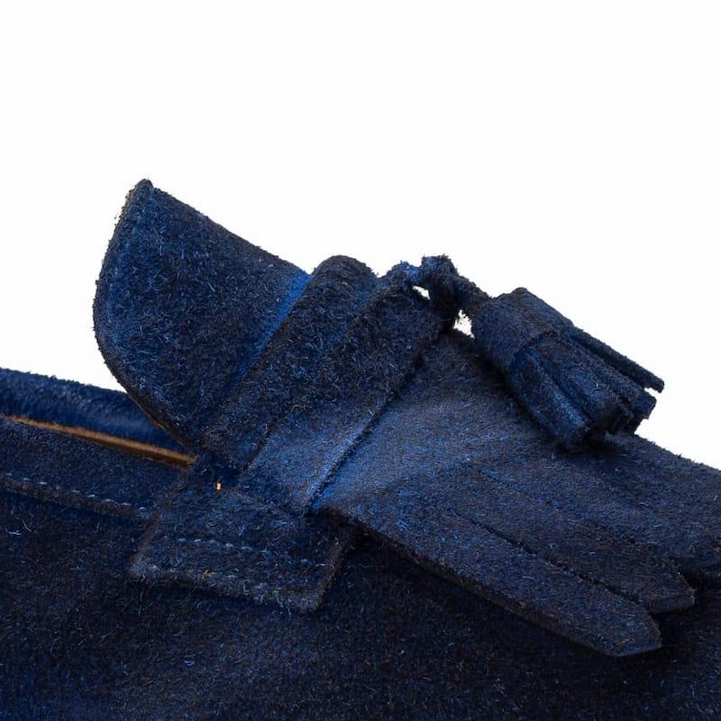 Puede incluir: Primer plano de un mocas&iacute;n de ante azul marino. El zapato presenta un detalle de borla y un aspecto suave y texturizado. El dise&ntilde;o es cl&aacute;sico y elegante, adecuado para diversas ocasiones.