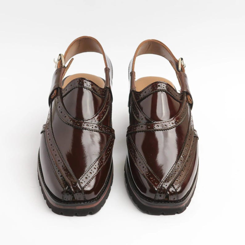 May include: A pair of brown leather shoes with a glossy finish. The shoes have a strap around the ankle and decorative perforations along the edges. The soles are dark brown, and the shoes appear to be new.