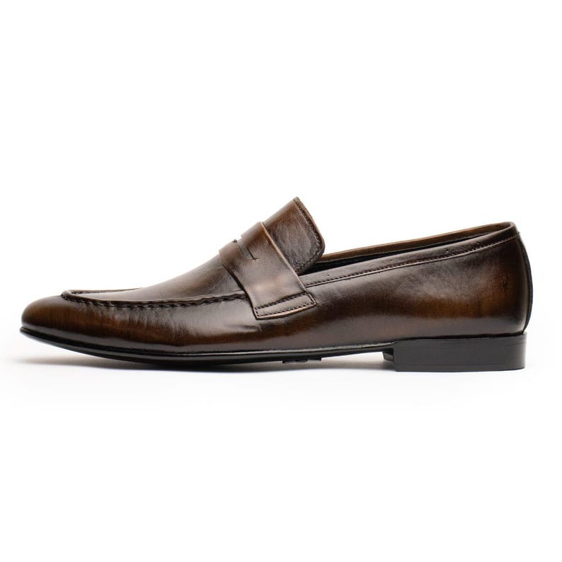 May include: A brown leather loafer shoe with a penny strap. The shoe has a rounded toe and a low heel. The leather has a polished finish and a slight sheen. The shoe is designed for formal or business wear.