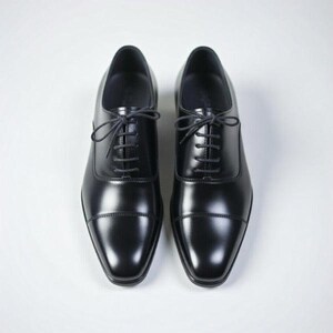 May include: A pair of black leather oxford shoes featuring a classic cap toe design, a smooth polished finish, and thin black laces threaded through five eyelets on each side. The shoes have a structured silhouette with a rounded toe box.