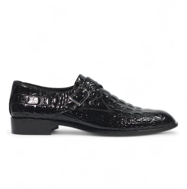 Puede incluir: Zapato negro de charol con textura de piel de cocodrilo. El zapato tiene un cierre de hebilla y un tac&oacute;n bajo. Adecuado para ocasiones formales.
