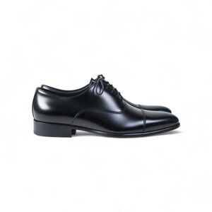 May include: A polished black leather oxford shoe featuring a classic cap toe design, a low stacked heel, and thin black laces. The shoe has a sleek, smooth finish with visible stitching along the toe cap and side panels, set against a plain white background.