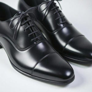 May include: A pair of black leather oxford shoes featuring a smooth, polished finish, a classic cap toe design, and thin black laces threaded through five eyelets on each side. The shoes have a structured silhouette with visible stitching details.