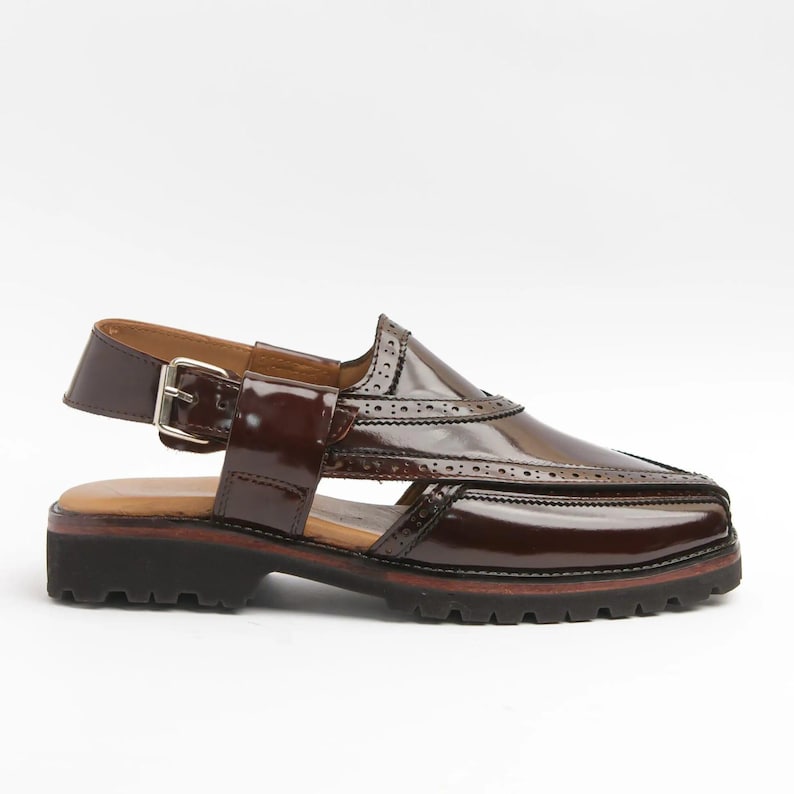 May include: A brown leather sandal with a glossy finish. The shoe features a buckle closure, decorative perforations, and a thick, lugged sole. The sandal has a unique design with a pointed toe and a slingback strap.