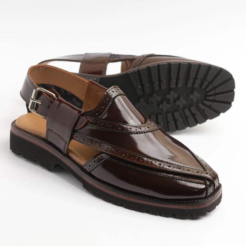 May include: Brown leather sandals with a glossy finish. The sandals feature a buckle closure, decorative perforations, and a thick, lugged sole. The design includes a strap around the ankle and a contrasting tan insole.