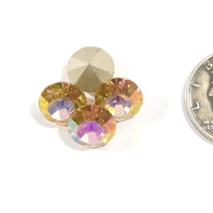 Puede incluir: Cuatro piedras de cristal de color dorado iridiscente con base plateada, junto a una moneda de diez céntimos para comparar el tamaño.