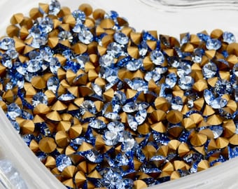 May include: A heart-shaped container filled with blue and gold rhinestones. The rhinestones are small and have a pointed shape.