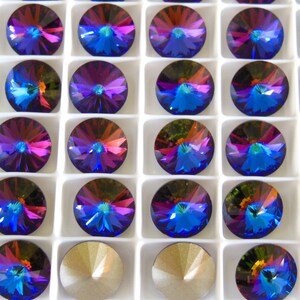 May include: A close-up view of a white tray filled with 36 iridescent blue, purple, and green round rhinestones. The rhinestones are arranged in a grid pattern.