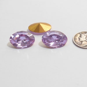 May include: Two light purple oval-shaped rhinestones and a gold-colored metal cone-shaped embellishment. The rhinestones are about the size of a dime.