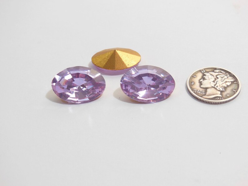 May include: Two light purple oval-shaped rhinestones and a gold-colored metal cone-shaped embellishment. The rhinestones are about the size of a dime.