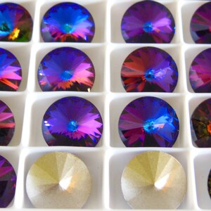 May include: A close-up view of a tray of round, iridescent purple and blue rhinestones. The rhinestones are arranged in a grid pattern and have a faceted design.