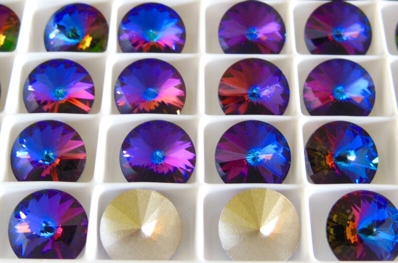 May include: A close-up view of a tray of round, iridescent purple and blue rhinestones. The rhinestones are arranged in a grid pattern and have a faceted design.