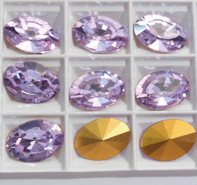 May include: A set of 8 oval-shaped rhinestones in a clear plastic container. The rhinestones are a light purple color and have a faceted design. There are also two gold-colored rhinestones in the container.