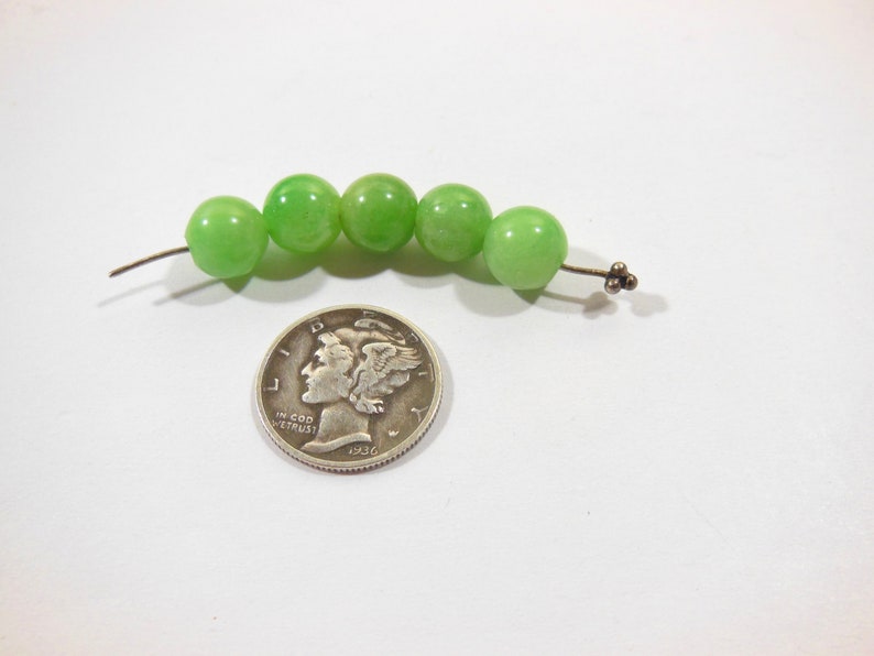 Op de afbeelding: Een streng van zes groene jade kralen geregen aan een zilveren draad met een zilveren sluiting.