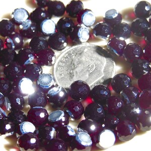 May include: A close-up of a pile of dark purple faceted glass beads. The beads are about the size of a US dime.