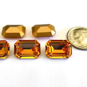 Puede incluir: Seis piedras de imitación de corte esmeralda en un cálido color ámbar. Las piedras de imitación están dispuestas en dos filas de tres. Se incluye una moneda de diez centavos de dólar estadounidense para comparar el tamaño.