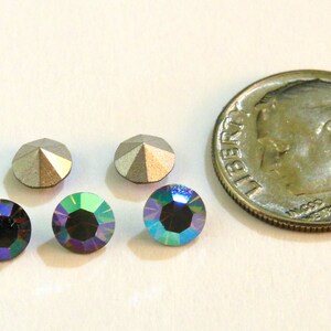 May include: Four iridescent blue-green rhinestones and two silver-toned rhinestones. The rhinestones are arranged in a row. A dime is included for size comparison.