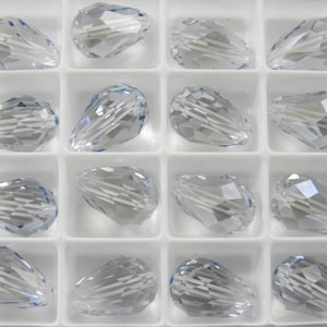 May include: A clear glass bead container with 16 teardrop-shaped beads. The beads are faceted and have a slight blue tint.