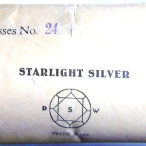 May include: A close-up of a cardboard box with the text "5 gross No. 24" and "STARLIGHT SILVER" printed on it. The box also features a registered trademark symbol and a diamond-shaped logo with the letters "D", "S", and "W" inside.