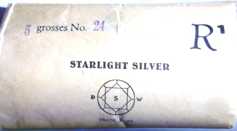 May include: A close-up of a cardboard box with the text "5 gross No. 24" and "STARLIGHT SILVER" printed on it. The box also features a registered trademark symbol and a diamond-shaped logo with the letters "D", "S", and "W" inside.