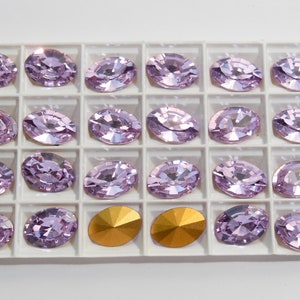 May include: A close-up of a white tray with 20 light purple oval-shaped rhinestones and two gold-colored rhinestones.