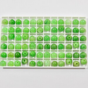 Op de afbeelding: Een witte lade met 64 kleine groene jade kralen in een rasterpatroon.