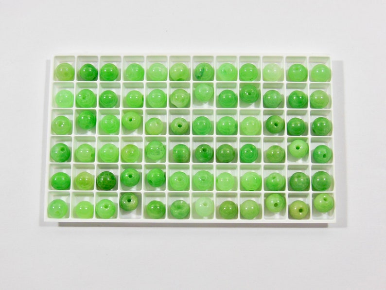 Op de afbeelding: Een witte lade met 64 kleine groene jade kralen in een rasterpatroon.