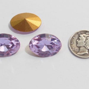 May include: Two light purple oval-shaped rhinestones with a gold-colored rhinestone in the background. The rhinestones are approximately the size of a US dime.