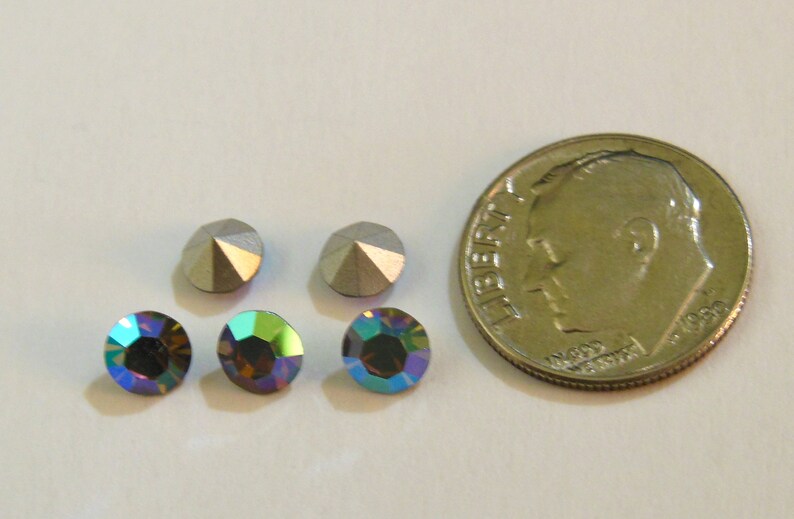 May include: Four iridescent rhinestones, two silver and two blue-green, next to a US dime coin for size comparison.