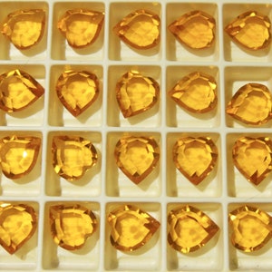 Puede incluir: Primer plano de una bandeja llena de 20 gemas de vidrio de forma de corazón, transparentes y de color ámbar. Las gemas están dispuestas en un patrón de cuadrícula.