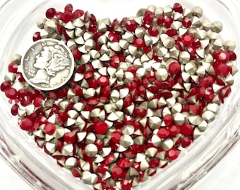 Puede incluir: Un plato de vidrio en forma de corazón lleno de pedrería roja y plateada. Se ve una moneda de plata en el plato. La pedrería es pequeña, facetada y refleja la luz. La moneda es una moneda de diez centavos Mercury de 1936.