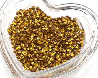 May include: A heart-shaped glass dish filled with gold-colored rhinestones. The rhinestones are small and have a pointed top.