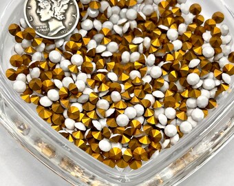 May include: A close-up image of a heart-shaped dish filled with gold and white rhinestones. The rhinestones are small and have a faceted design.