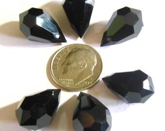 May include: Six black, faceted, teardrop-shaped beads arranged around a silver coin. The beads have a glossy finish and a small hole for stringing. The coin shows a profile of a man.