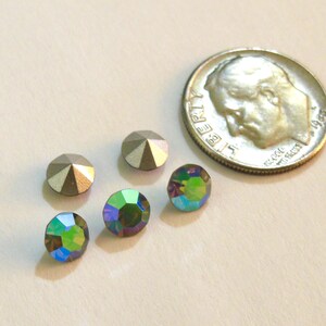 May include: Five rhinestones, two silver and three iridescent green, are arranged on a white surface next to a US dime for scale.
