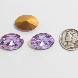 May include: Two oval-shaped, light purple rhinestones with a gold-toned base. The rhinestones are approximately the size of a US dime.