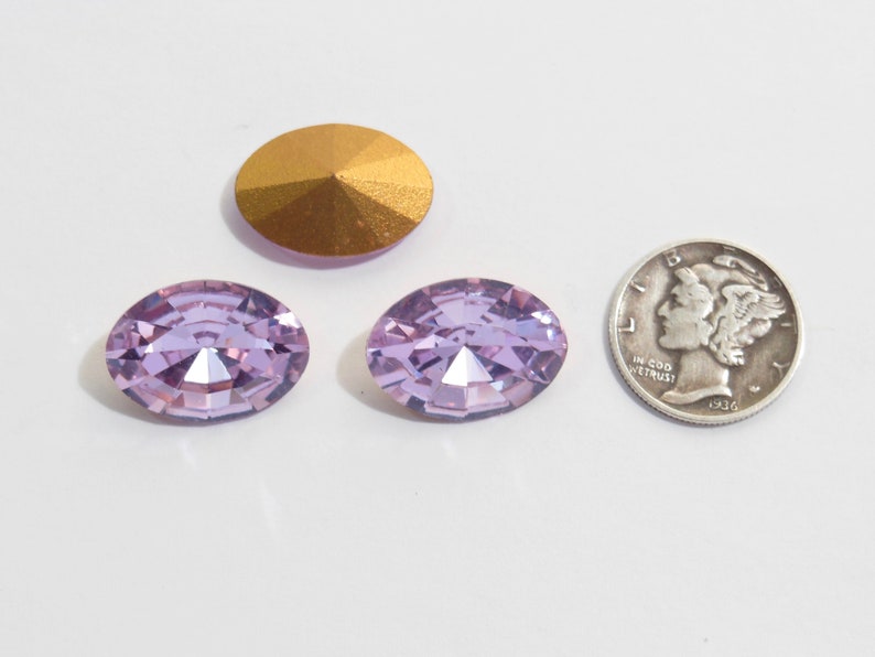 May include: Two oval-shaped, light purple rhinestones with a gold-toned base. The rhinestones are approximately the size of a US dime.